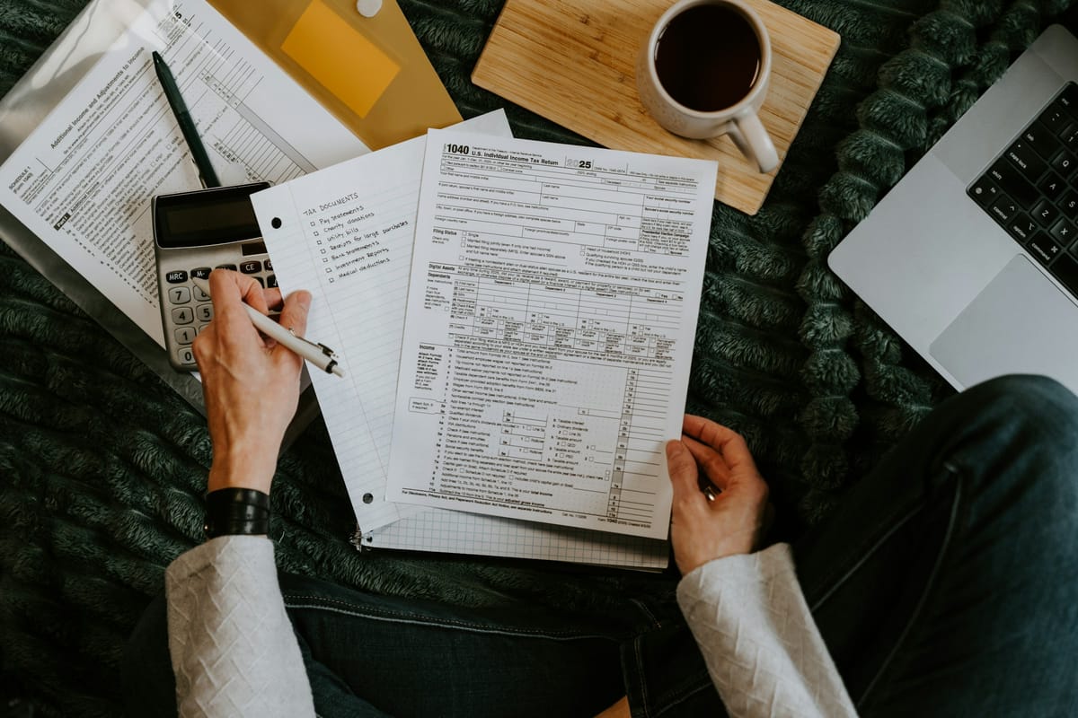 A person reviews financial paperwork beside a calculator and laptop.