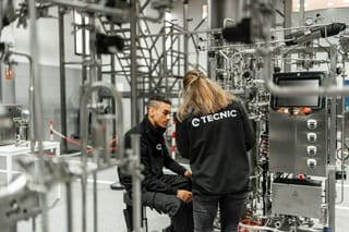 Two technicians inspect stainless-steel bioprocess equipment.