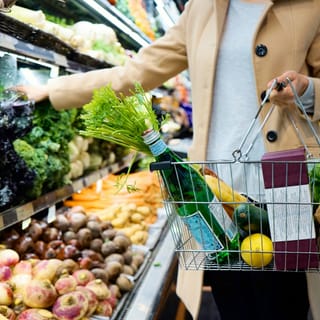 A shopper holds a wire grocery basket beside fresh produce in a supermarket.