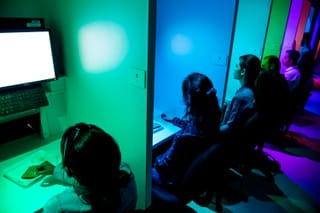 People assess food samples in individual booths at a sensory science centre under coloured lighting.